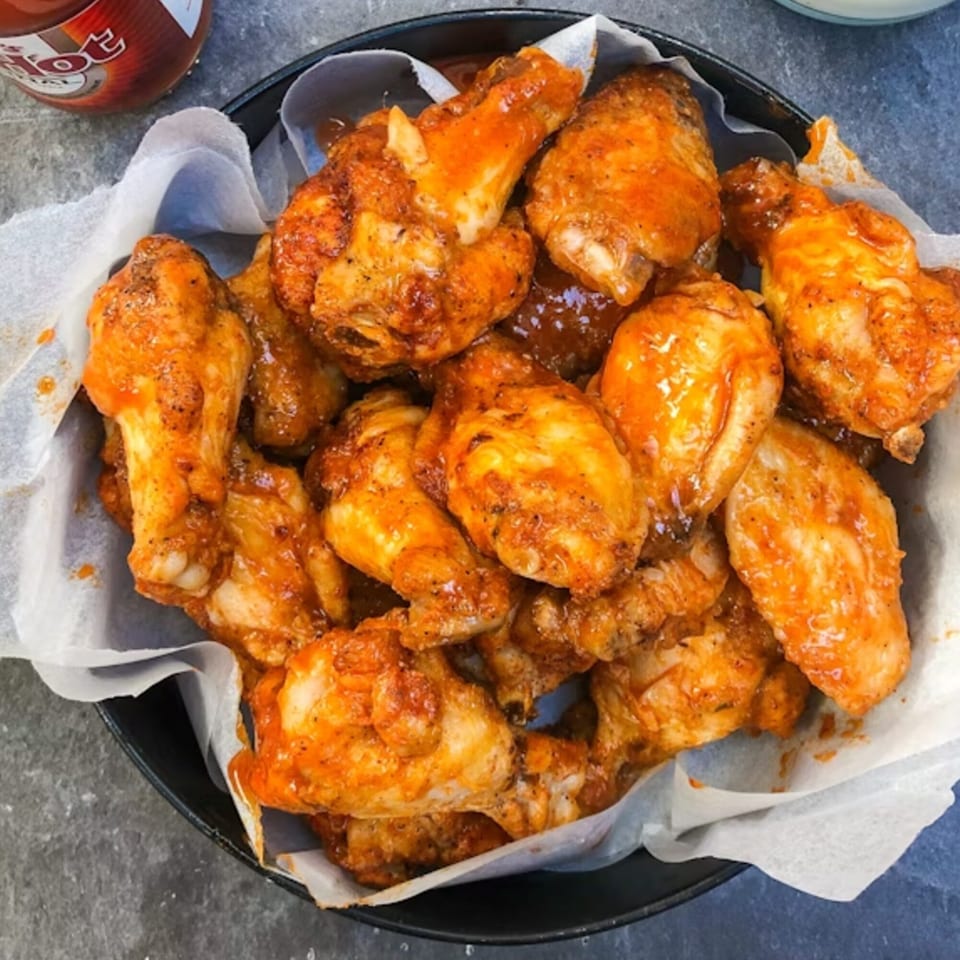 A black bowl filled with Main St Pizza & Ice Cream's hot, saucy chicken wings on parchment paper.