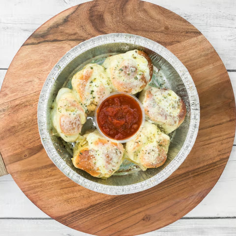 Cheesy garlic knots with marinara sauce in a foil pan, on a wooden board.
