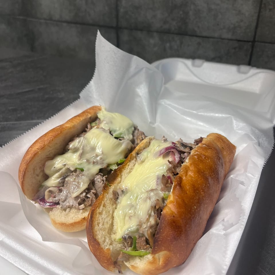 Two cheesy steak and onion subs in a white takeout container from Main St Pizza.