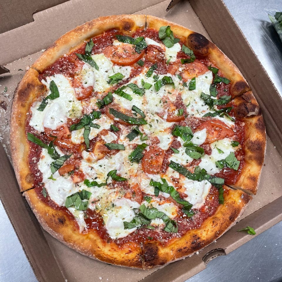 A freshly baked Main St Pizza & Ice Cream Margherita pizza with basil, mozzarella, and tomatoes in a box.