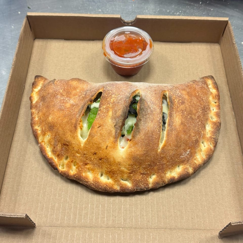 A golden-brown calzone with visible fillings and a side of marinara sauce in a pizza box.
