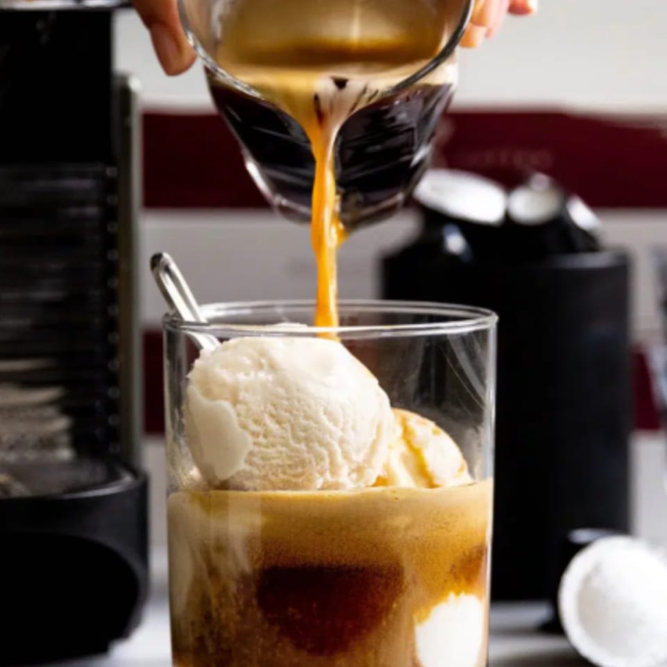 Espresso pouring from a glass into a tall glass with scoops of vanilla ice cream.