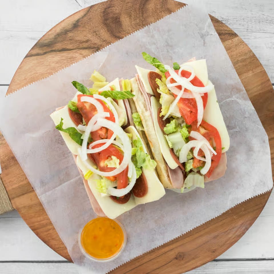 Two halves of a loaded sub sandwich with meats, cheese, lettuce, tomatoes, and onions.